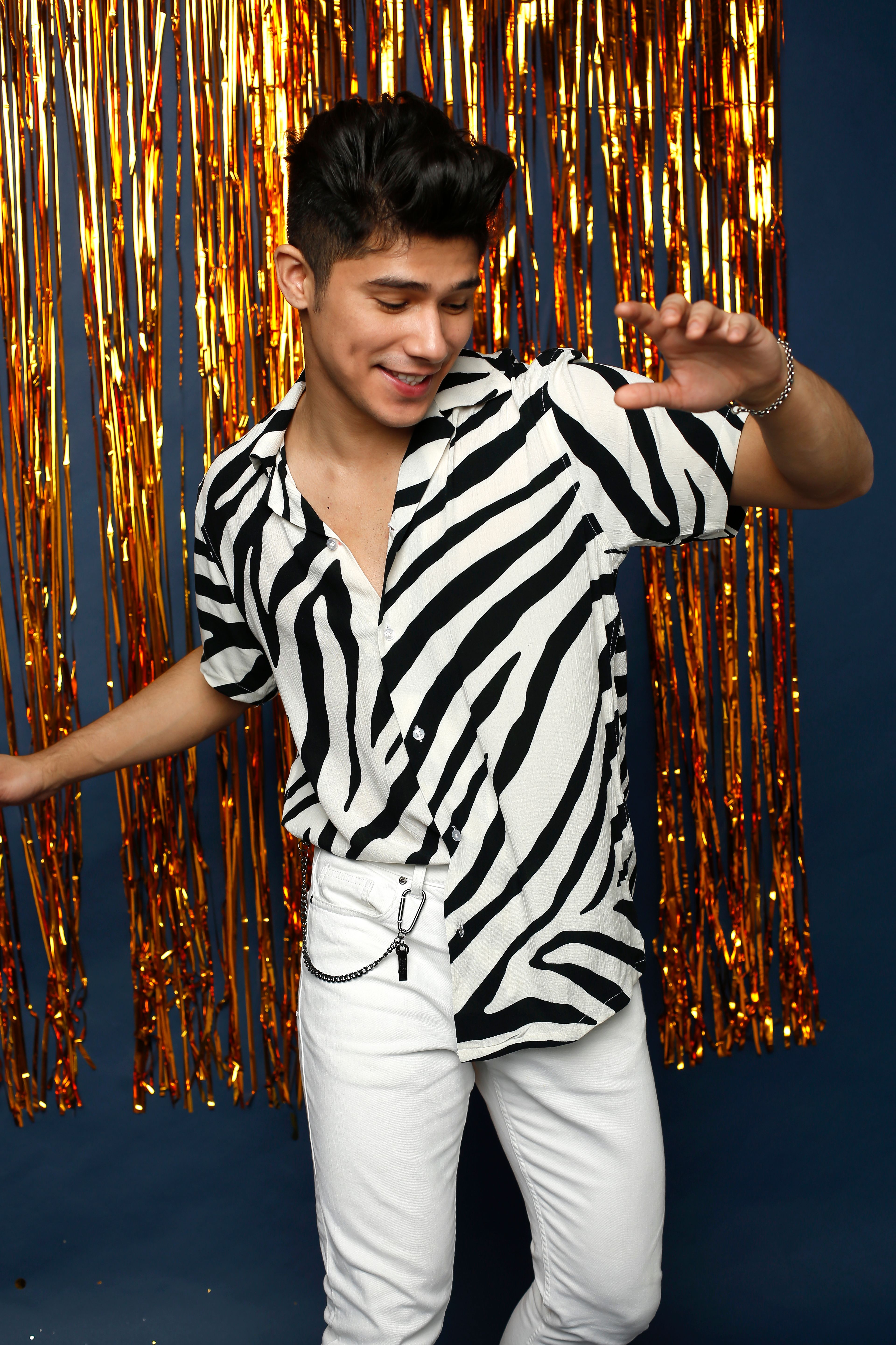 A fashionable man poses joyfully in a zebra print shirt against a shimmering foil curtain.