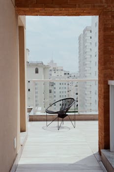 Minimalist balcony with chair and cityscape view on a sunny day.