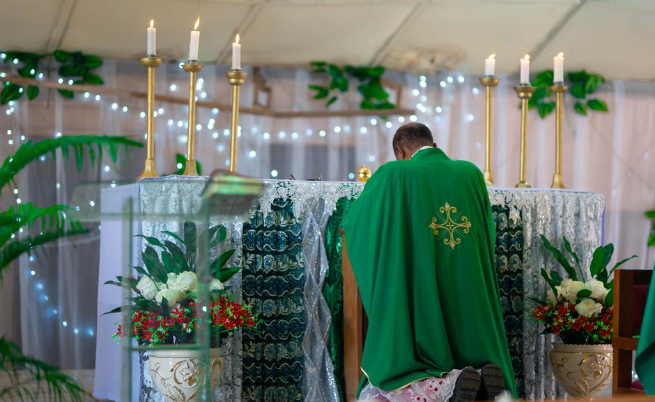 Preot în veșminte verzi la altar decorat cu flori și lumânări de Rusalii