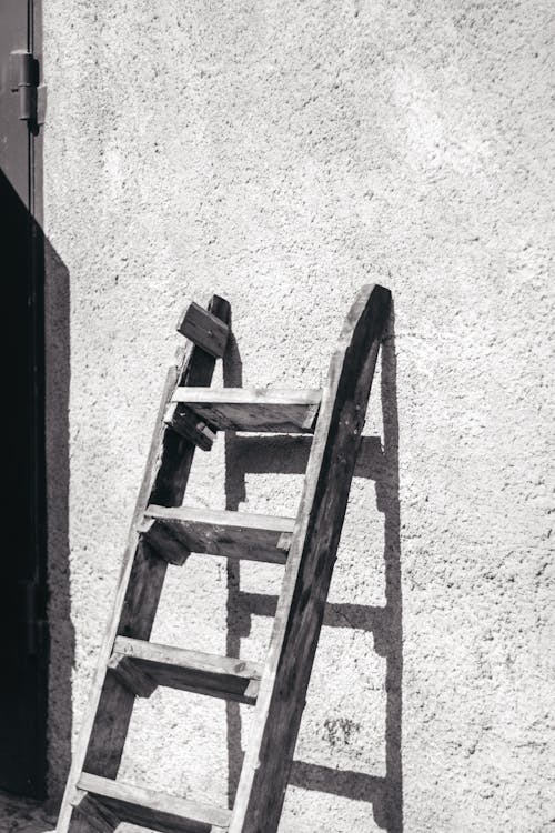 Grayscale Photo of a Wooden Ladder Leaning on a Wall