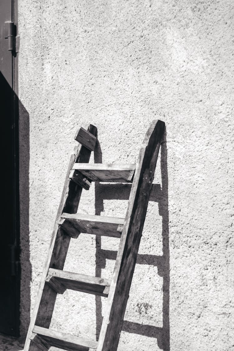 Grayscale Photo Of A Wooden Ladder Leaning On A Wall