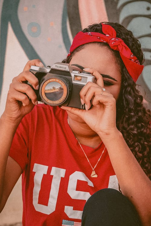 Close-Up Shot of a Woman in Red Shirt Taking Photos Using an Analog Camera