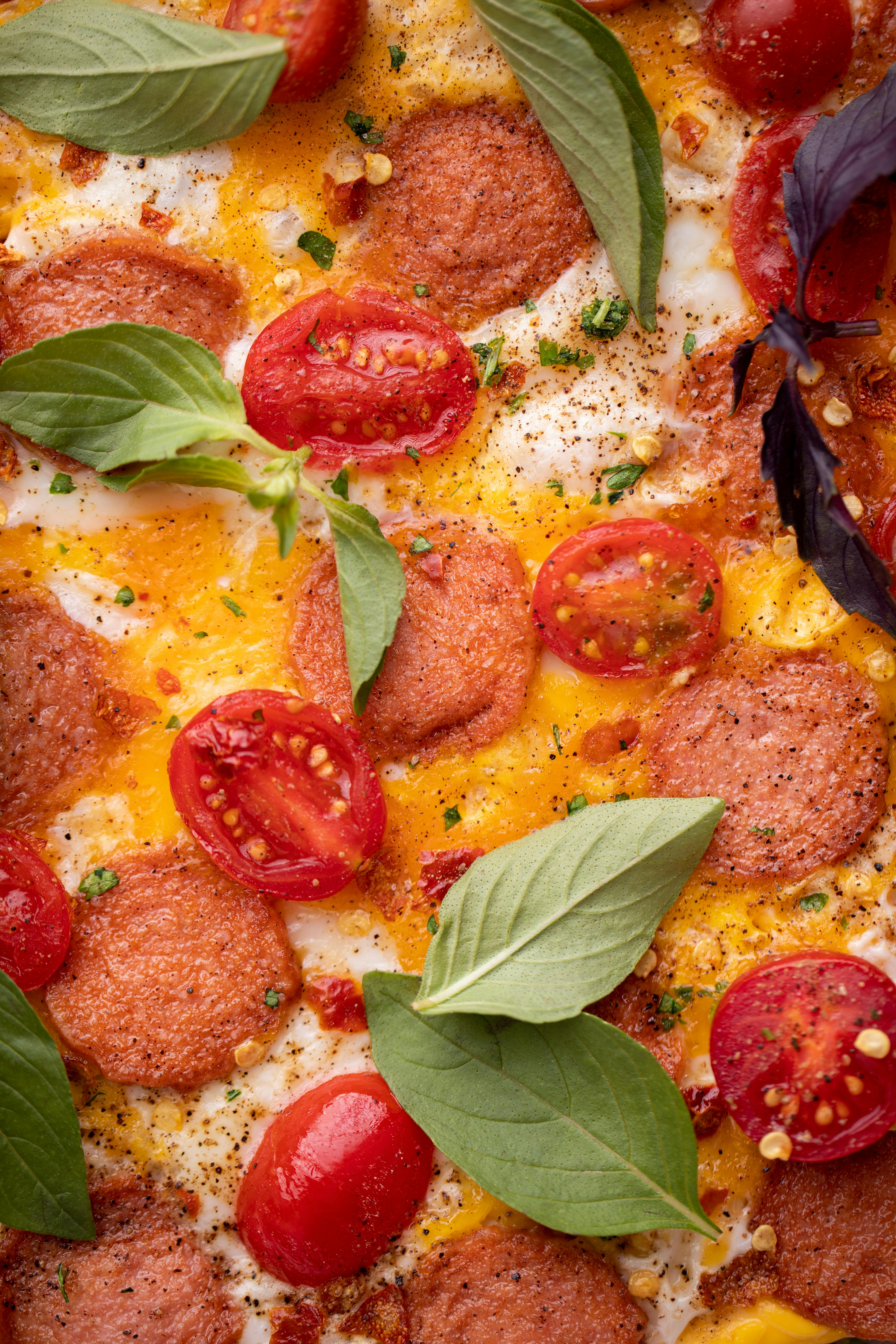 Close-up view of a freshly baked pizza with pepperoni, tomatoes, and basil leaves.