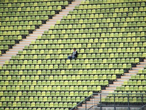 Free Woman in Grey Shirt Sitting on Stadium Chair Stock Photo