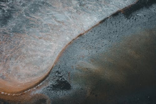 Drone view of peaceful landscape of wavy sea water washing wet sandy beach in daytime
