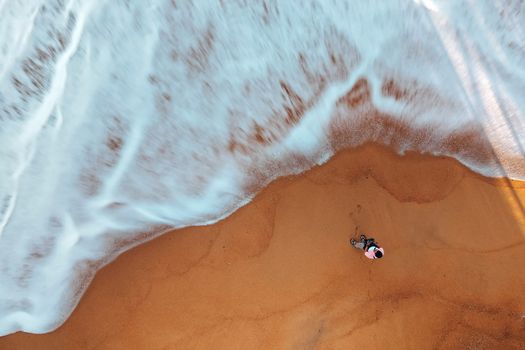Drone view of anonymous male travelers standing on sandy beach and admiring picturesque foamy ocean while launching UAV
