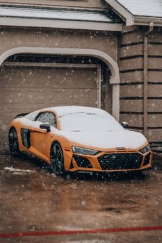 Luxury sports car covered in snow parked in a driveway during winter snowfall.