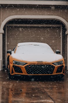 Orange Audi sports car parked in front of a garage, covered in snow during winter.