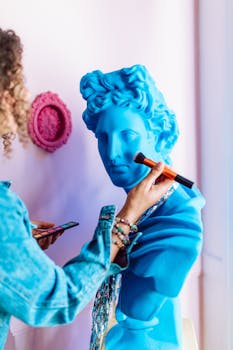 A person applying makeup to a vibrant blue statue indoors, showcasing creativity.