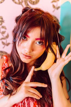 Colorful portrait of a young woman creatively using a banana as a phone, featuring vibrant makeup and expressive styling.
