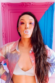 Artistic portrait of a young woman blowing bubblegum with vivid makeup and modern style.