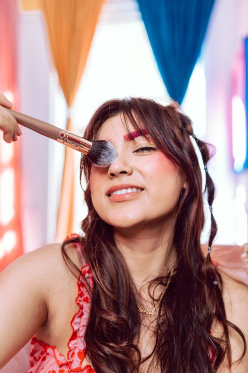 Free A smiling woman getting makeup applied with a brush. Bright and colorful setting. Stock Photo