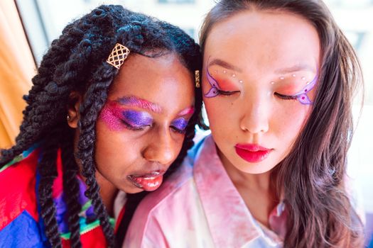 A colorful and artistic portrait highlighting vibrant makeup and fashion-forward style of two young women.