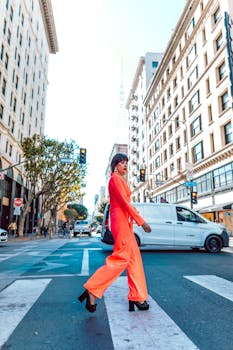 Fashionable woman in bright orange outfit crossing an urban city street.