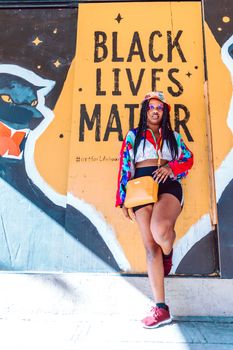 Stylish woman poses confidently against a Black Lives Matter mural in a vibrant urban setting.