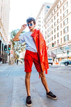 Trendy young adult showcasing vibrant street fashion with a red jacket and sunglasses in a city setting.