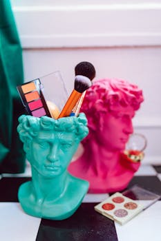Vibrant makeup tools in colorful bust sculptures create a striking still life composition.