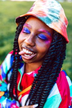 Colorful portrait of a woman outdoors with braided hair, creative makeup, and a tie-dye bucket hat.
