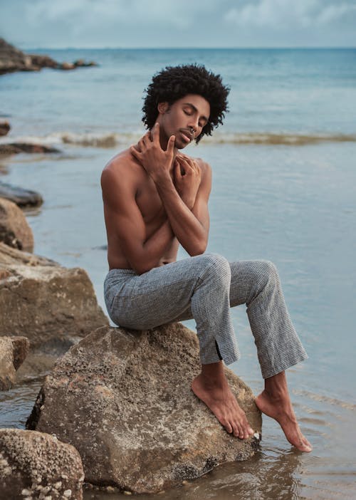 Gentle black man sitting on stony shore of sea