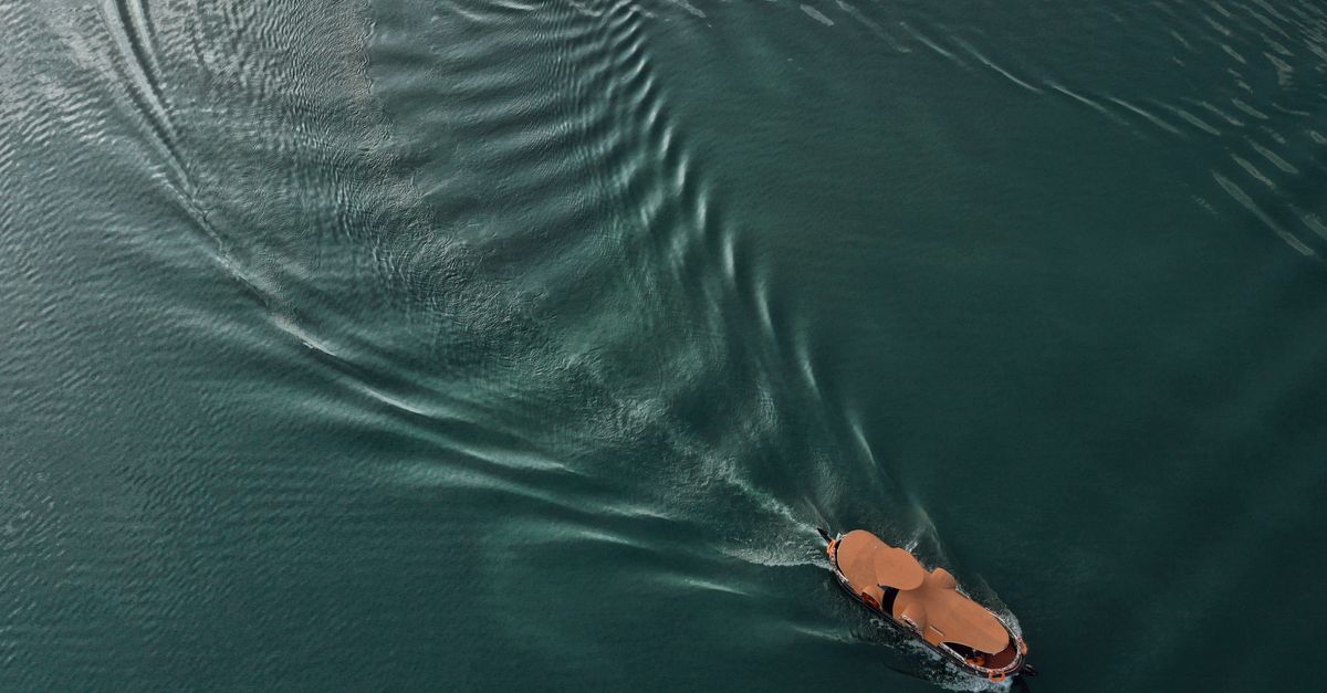Drone view of brown vessel sailing on calm dark green ocean and leaving mark on water surface