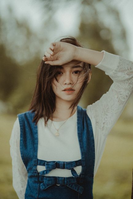 A young woman posing with her hand on her forehead in a serene outdoor setting.