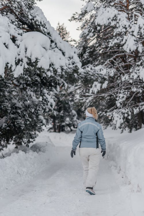Back View of a Woman in a Blue Jacket Walking on a Snow Covered Pathway