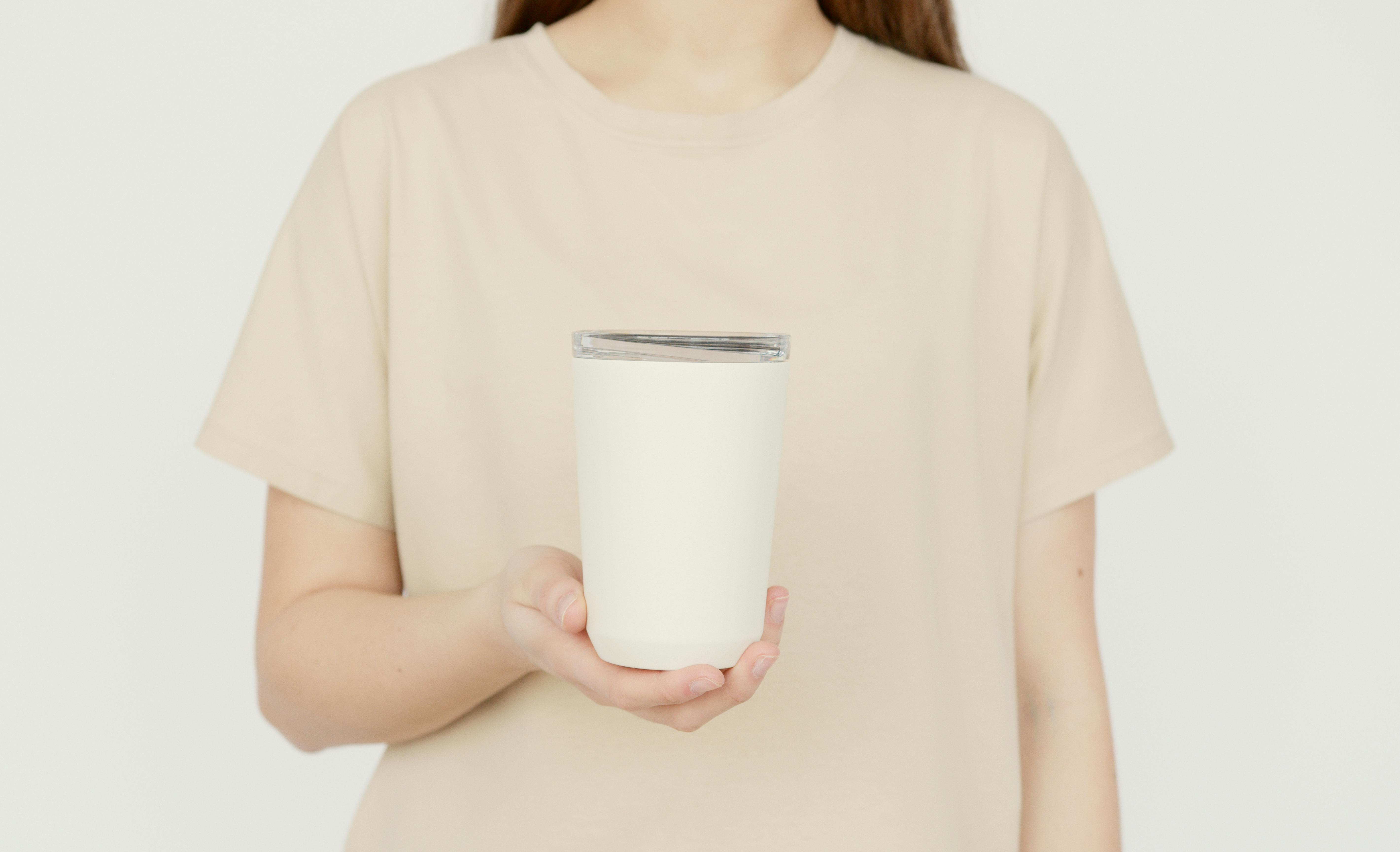 Young adult in a beige t-shirt holding a blank white tumbler against a neutral background.