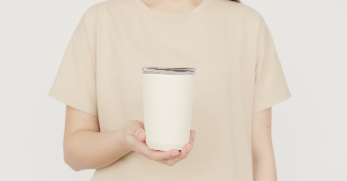 Young adult in a beige t-shirt holding a blank white tumbler against a neutral background.