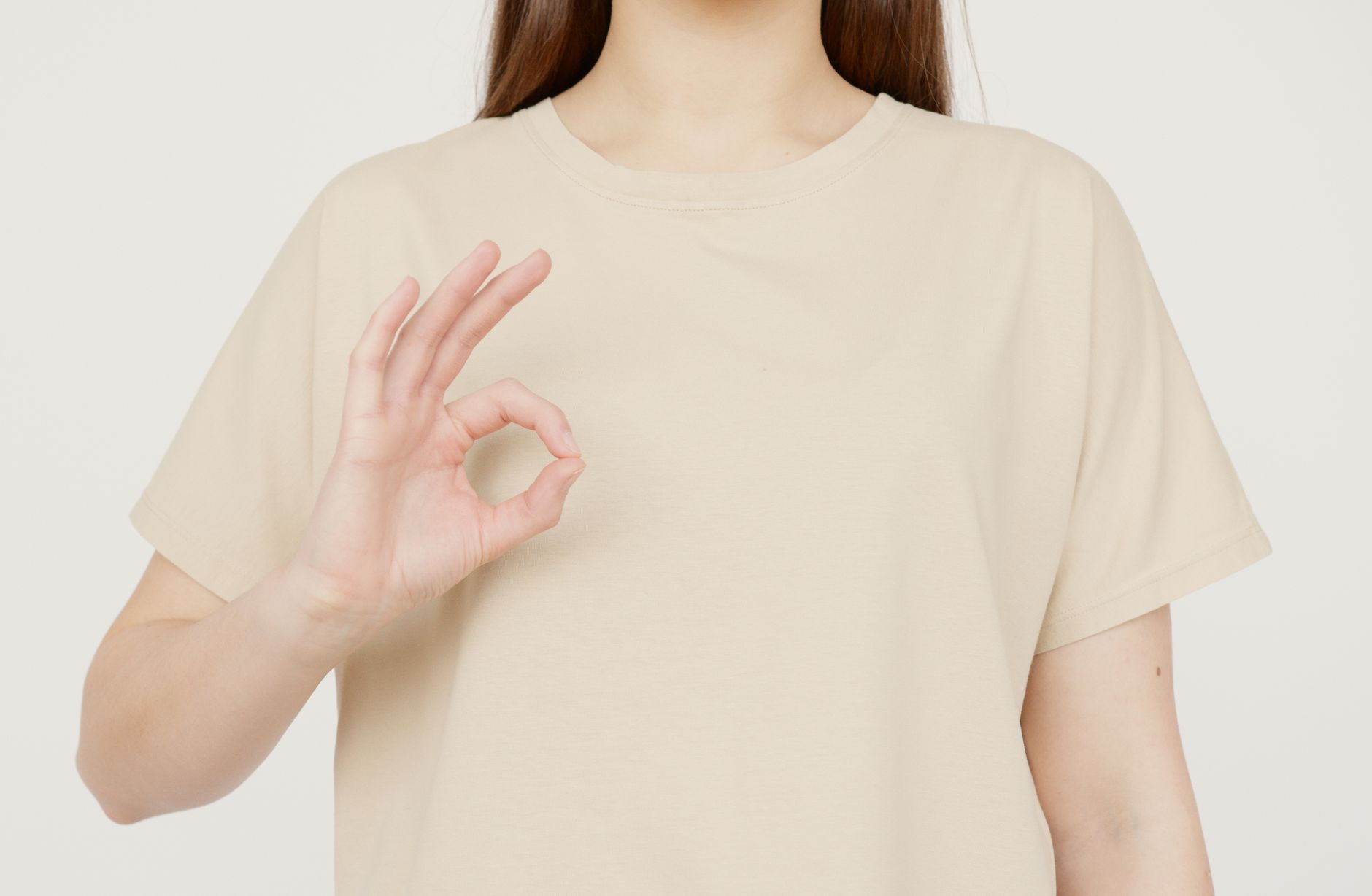 Close-up of a woman in a beige t-shirt making an okay gesture with her hand. Perfect for concepts of approval, satisfaction, and positivity.