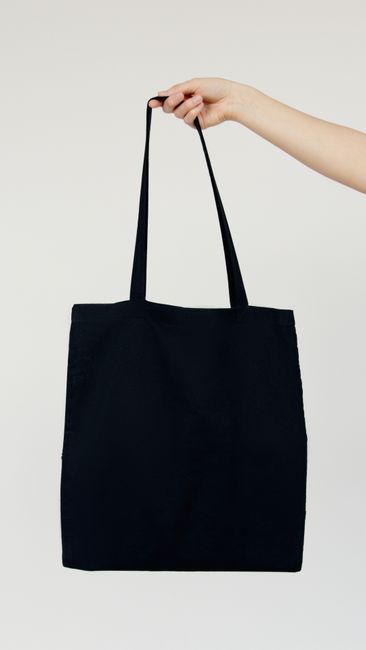 Minimalist image of a hand holding a blank black tote bag against a neutral background. - handbag care tips
