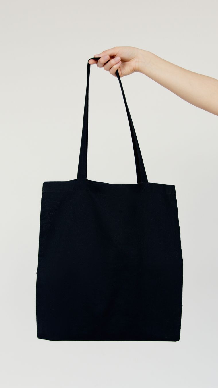 Hand holding a plain black cotton tote against a neutral wall - photo by Artem Podrez on Pexels