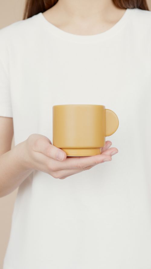 Free Closeup of a woman in casual wear holding a yellow mug against a neutral background. Stock Photo