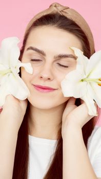 Smiling woman with white flowers and a headband against a pink background, eyes closed in serenity.
