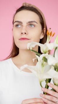 Portrait of a woman holding white Madonna lilies against a pastel pink backdrop.