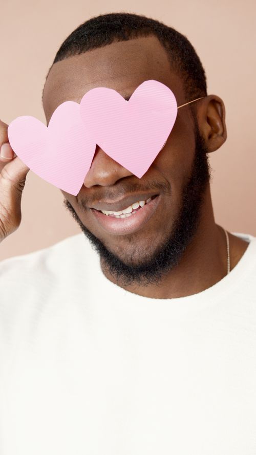 Free Portrait of a smiling man wearing pink heart-shaped paper glasses over his eyes. Stock Photo