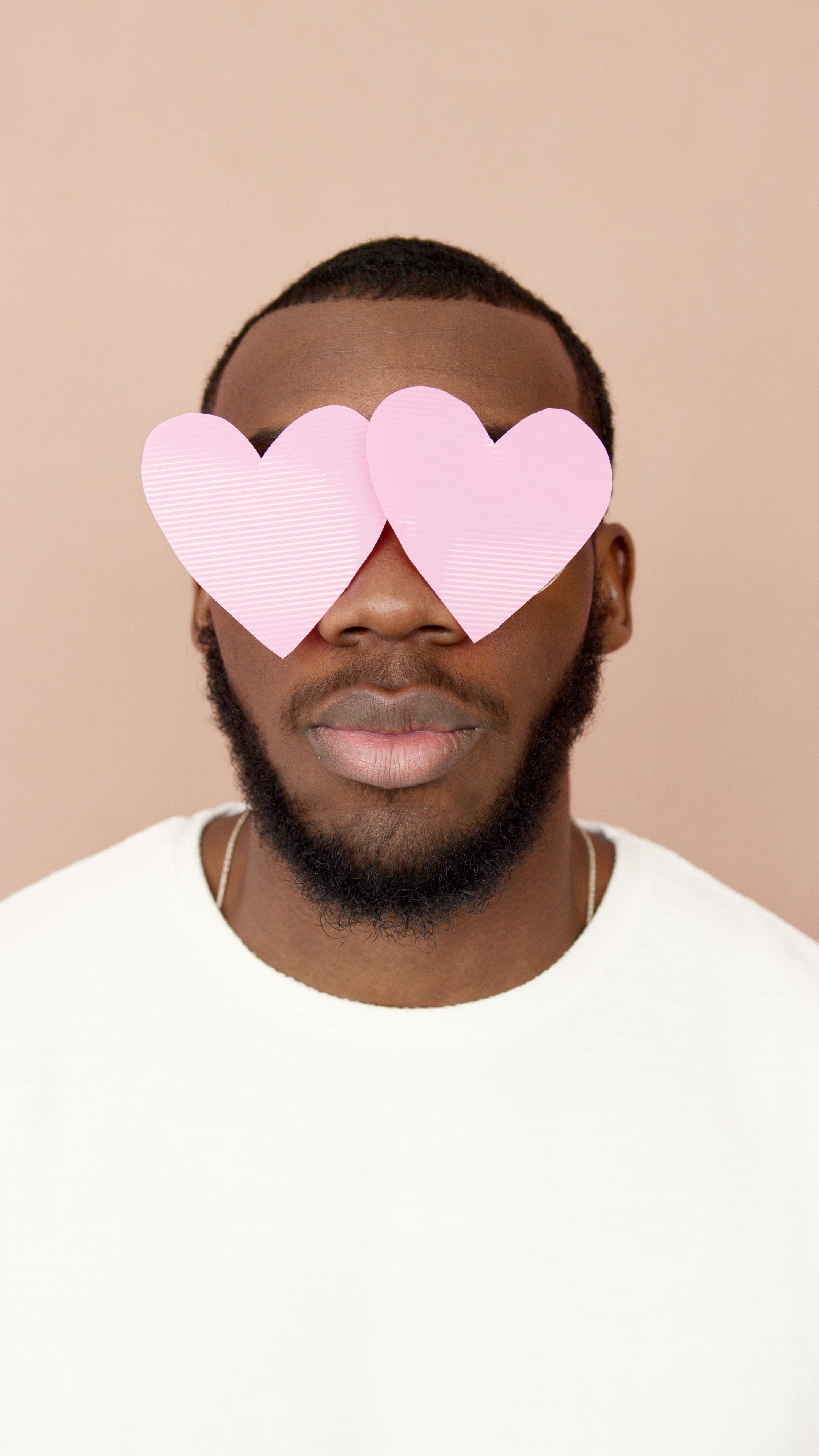 A creative portrait of a man with pink heart-shaped paper cutouts covering his eyes.