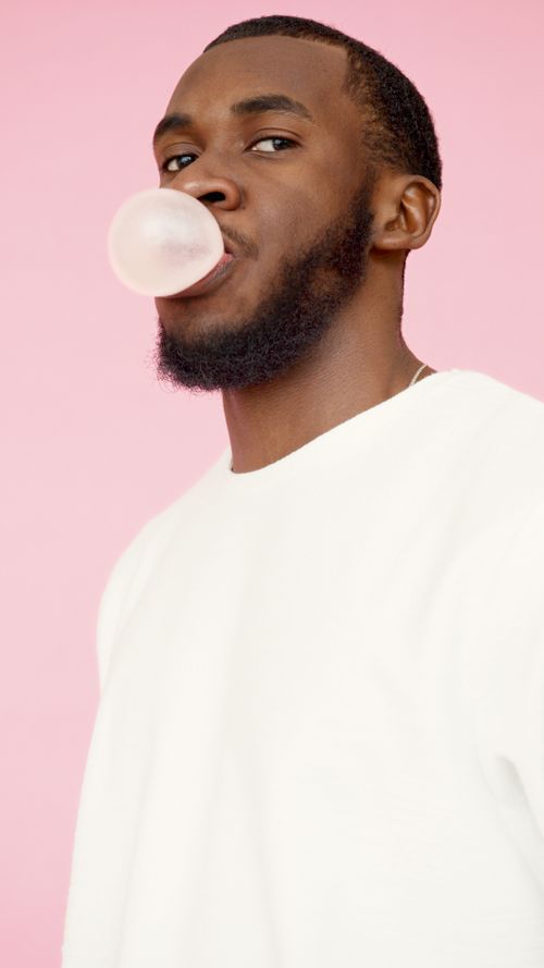 Free Fashionable bearded man blowing bubblegum against a pastel pink background. Stock Photo