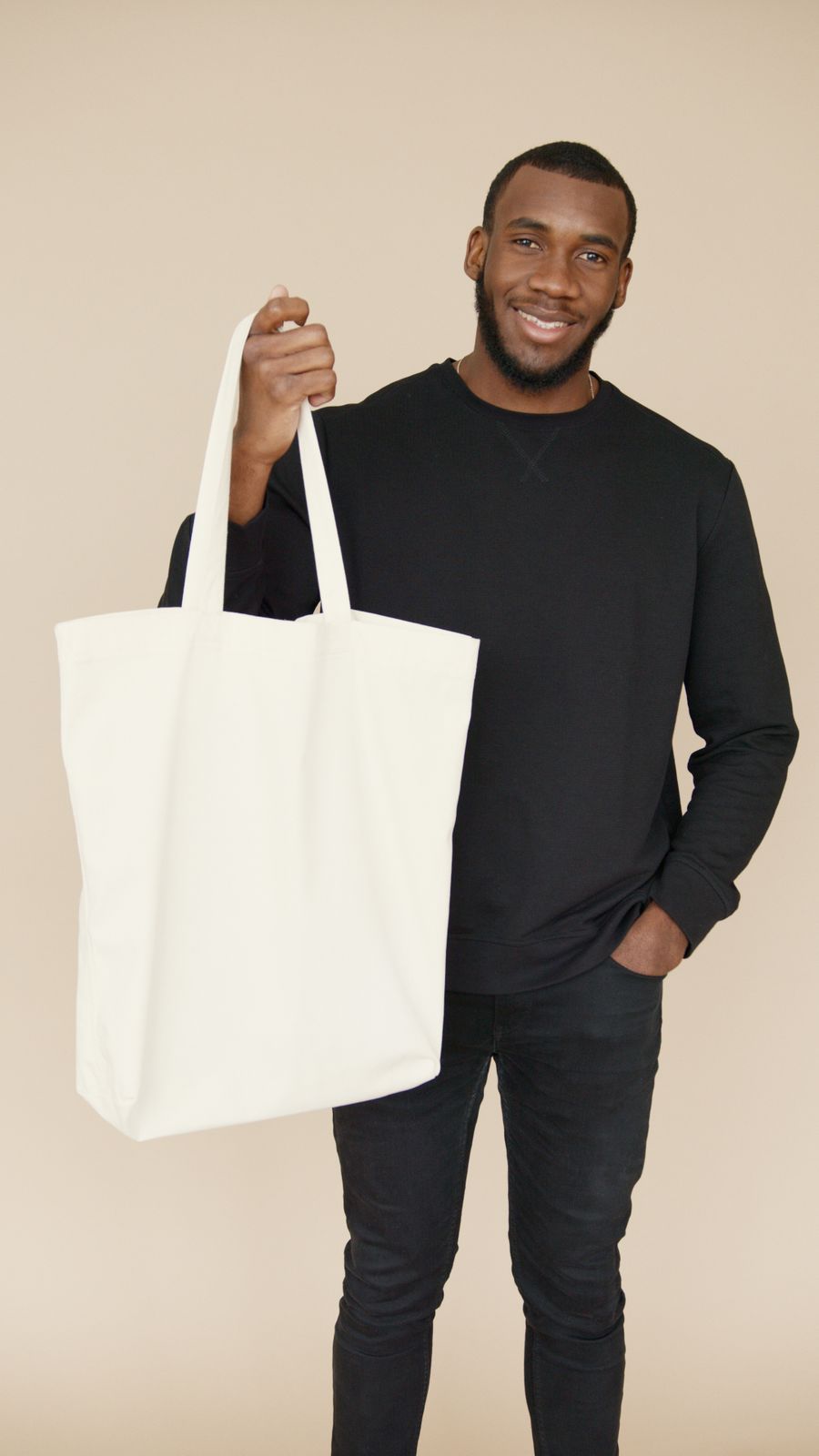 Person holding a blank canvas tote against a plain backdrop - photo by Artem Podrez on Pexels