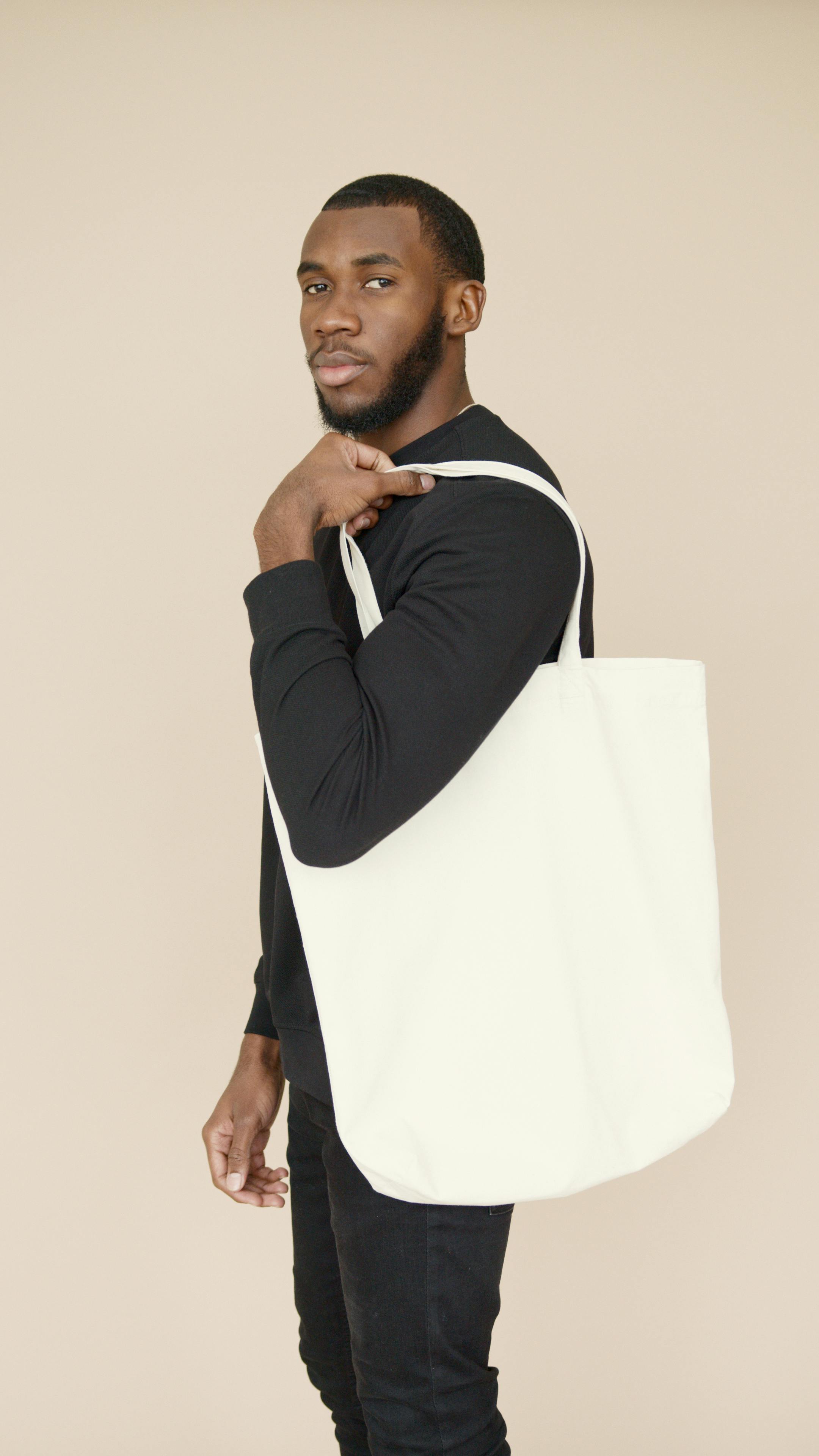 bearded man in black clothing holding a white shopping bag