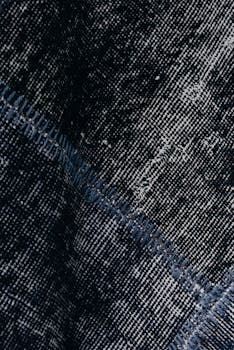 Detailed close-up of textured dark denim fabric with visible stitching pattern.