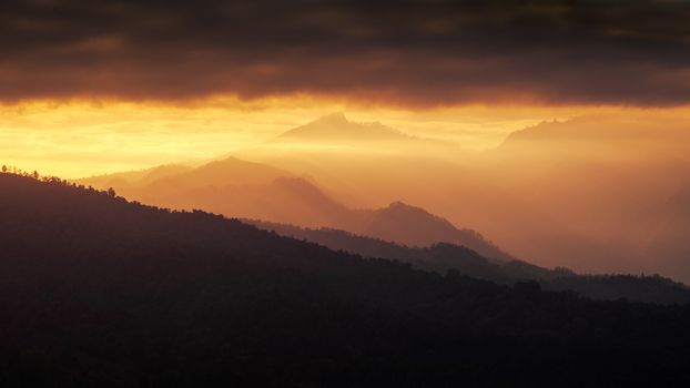 Serene mountain range silhouette at golden sunset with dramatic clouds and vibrant sky.