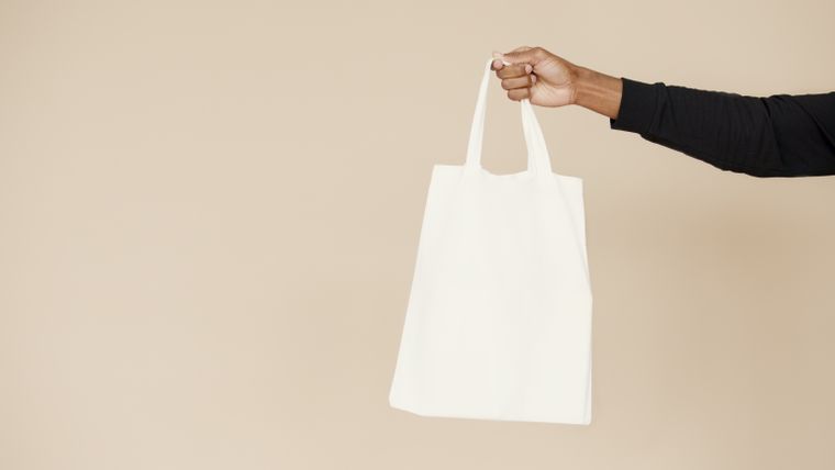 Plain white cotton tote held up against a neutral wall - photo by Artem Podrez on Pexels