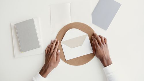 Free Overhead shot of hands arranging an envelope among notebooks on a minimal workspace. Stock Photo