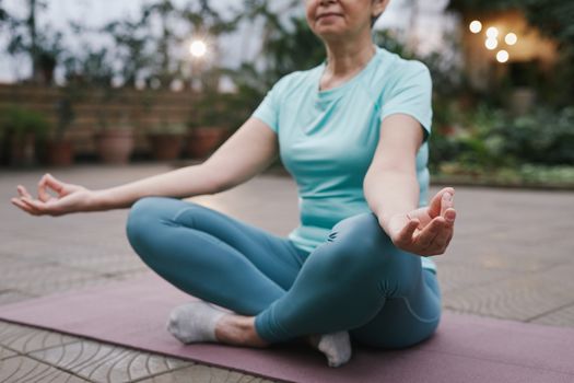 Elderly woman practicing yoga meditation outside in a serene setting.