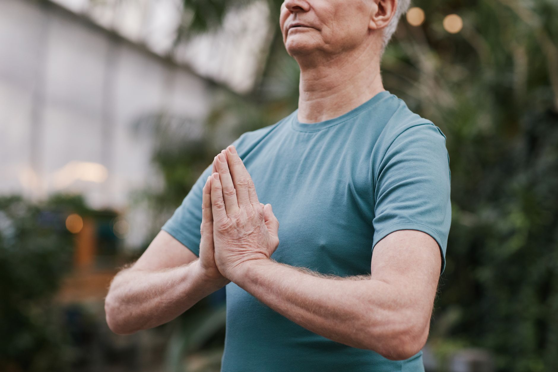 Senior man in a blue t-shirt practicing yoga indoors, focusing on mindfulness and peace.