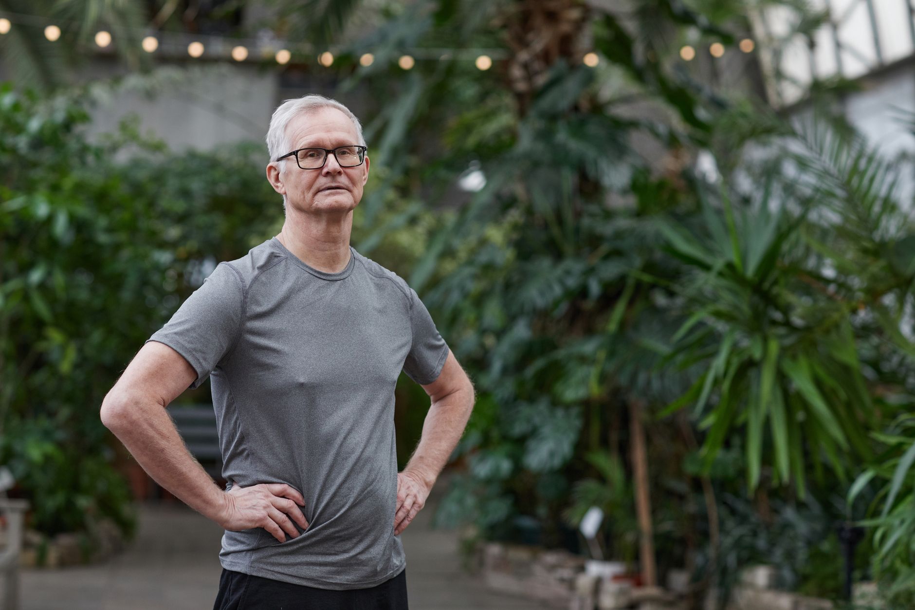 Elderly man in sportswear standing confidently among lush greenery.