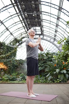 A senior man practicing yoga in a botanical garden greenhouse, surrounded by lush greenery.
