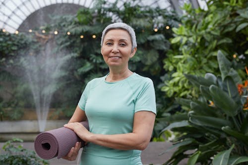 Free Woman Smiling While Holding a Yoga Mat Stock Photo