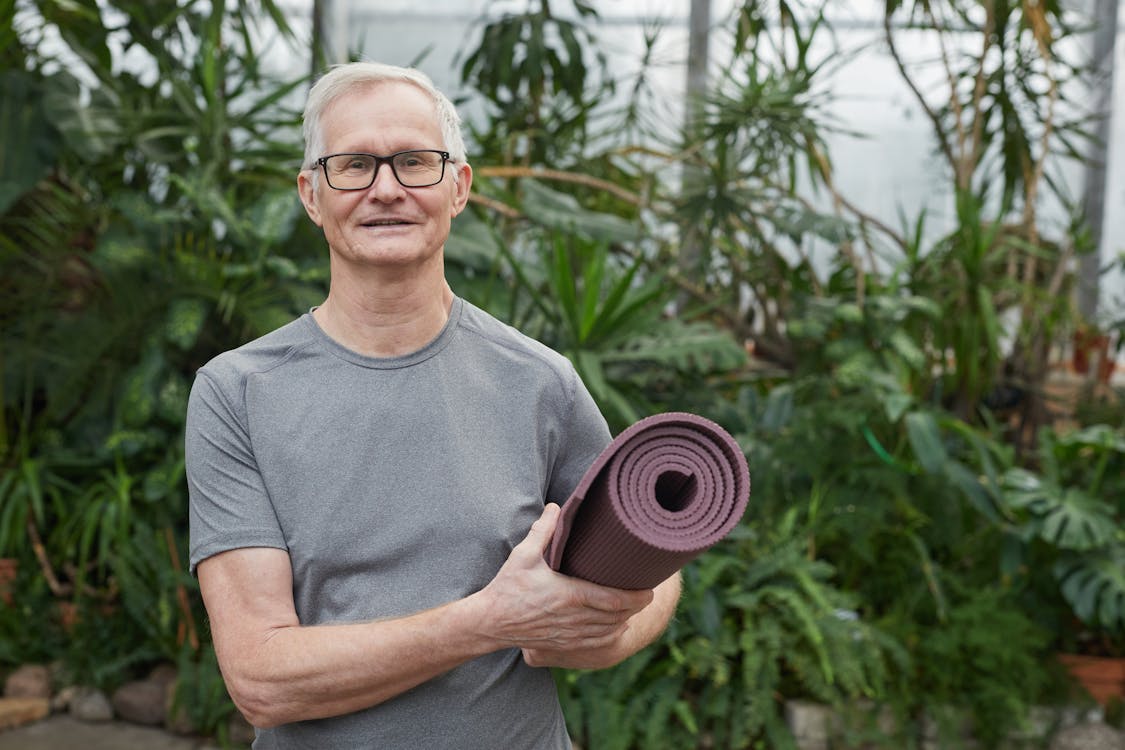 Free Man Standing While Holding a Yoga Mat Stock Photo