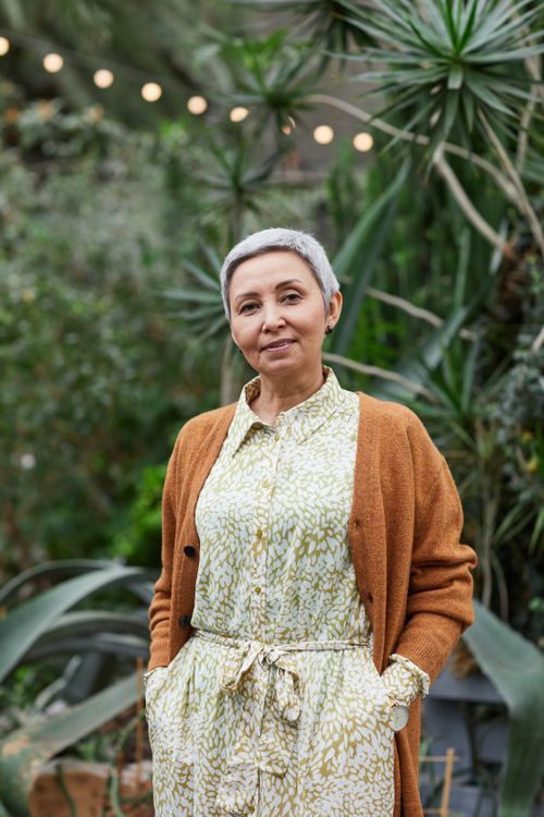 Free Portrait of an elegant senior woman smiling in a lush garden setting. Stock Photo